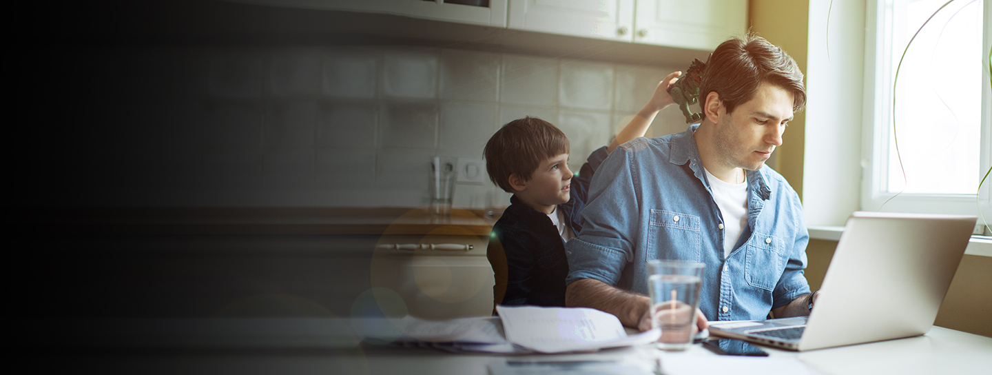 man working on computer while boy play with toy on his head